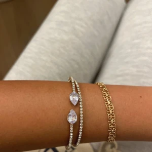 Glittrigt armband med droppformade stenar - Säljer ett snyggt armband i silverfärg med två rader av gnistrande stenar och två stora droppformade kristaller. Perfekt för dig som gillar bling och vill sticka ut med ett elegant smycke som fångar ljuset.
