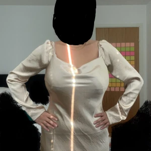 Champagnefärgad satin klänning - Snygg midiklänning i satin/siden från Asos i champagnefärg. Materialet är glansigt och känns lyxigt, klänningen är oanvänd. Lite defekter som man ser på bild 3.