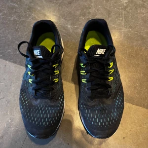 Nike svarta löparskor med gula detaljer - Snygga svarta Nike löparskor med vit swoosh och coola gula detaljer på snörningen. Ovandelen är i mesh för bra andningsförmåga och sulan är vit med gul kant. Perfekta för dig som gillar att sticka ut på löprundan eller på gymmet. Storlek 42. 