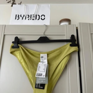 Glittriga limegul bikiniunderdel H&M -  bikiniunderdel från H&M i en fräsch limegul färg med glittrig finish. Modellen har klassisk midja och är tillverkad i mjuk polyester som känns bekväm mot huden. 