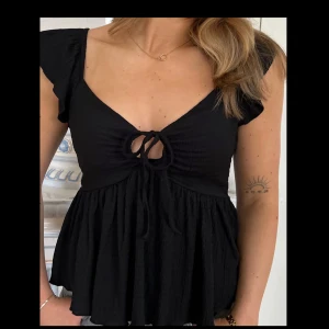 Svart topp med knyt - Supersöt svart topp från lager som heter Felicity. Oanvänd och har slutat säljas i denna färg på hemsidan. Första bilden är lånad från deras Facebook och den sista bilden hitta jag sen gammalt från Google då den inte längre finns på hemsidan!