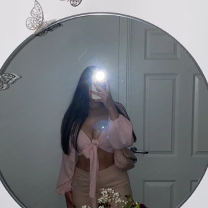 Ljusrosa omlott blus med knyt - Säljer en superfin ljusrosa blus med omlott och knyt framtill. Toppen har långa, lite puffiga ärmar och är croppad så magen syns. Perfekt för dig som vill ha en söt och trendig look med romantiska vibes.