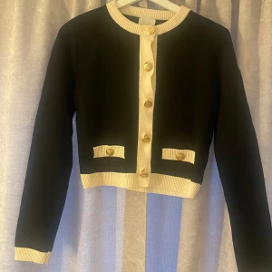 Svart kofta med gulddetaljer - Snygg svart kofta med vita ribbade detaljer, guldiga knappar framtill och vid fickorna ger en lyxig känsla. Perfekt till jeans eller kjol🩷🩷