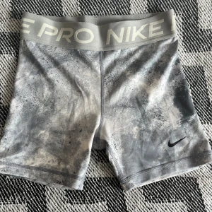 Nike Pro Dri-Fit grå träningsshorts - Nike Pro Dri-Fit shorts i grått och vitt med coolt mönster och bred resår i midjan med NikePro-logga. Tight passform och tillverkade i funktionsmaterial som andas, perfekta för träning eller sport. Snyggt tryck och klassisk Nike-detalj på benet. Det är barnstorlek alltså L/146-156. 🎾🥅⚽️