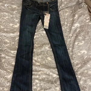 Mörkblå bootcut jeans från Basic Jeans - Snygga mörkblå jeans från Basic Jeans med bootcut passform. Jeansen har klassiska gula kontrastsömmar och coola detaljer på bakfickorna. Tillverkade i jeansmaterial med en stilren look som passar till det mesta. De har aldrig använts 