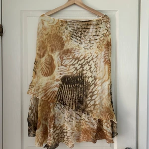 Vintage volangkjol - Säljer en flowy vintage kjol från Life Style i beige och bruna toner. Kjolen har ett unikt abstrakt mönster med snäckskalsvibbar och är tillverkad i ett lätt material. Perfekt för dig som gillar boho-stil och vill ha något som sticker ut. Passar från M. 