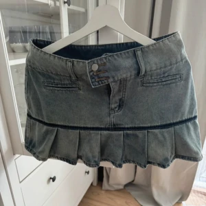 Jeanskjol med volangkant - Snygg kort jeanskjol i blå denim med volangkant nedtill och dubbla knappar i midjan. Kjolen har bälteshällor och dekorativa fickor fram. Perfekt för en trendig och avslappnad look.