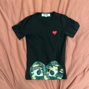 Svart Comme des Garçons Play t-shirt - Svart t-shirt från Comme des Garçons Play med klassiskt rött hjärta på bröstet och stora ögon i camouflageprint längst ner. T-shirten är i storlek S, men skulle säga att den passar xs bättre. Vid frågor eller  funderingar är det bara att skriva. Pris  går att sänkas 😁