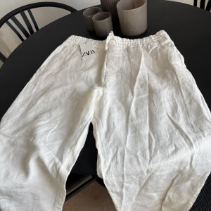 Vita linnebyxor från Zara - Snygga och luftiga vita linnebyxor från Zara med elastisk midja och snörning. Perfekta för varma dagar, med avslappnad passform och sidfickor. Stilrena och enkla att matcha till olika looks.
