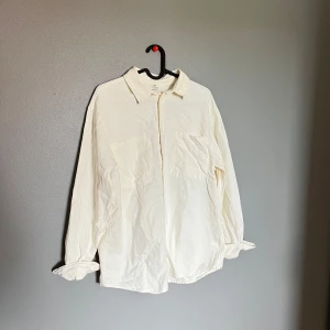 Vit overshirt från H&M i bomull - Stilren vit overshirt från H&M i 100% bomull. Skjortan har klassisk krage, två stora bröstfickor och knäppning framtill. Långärmad modell med avslappnad passform, perfekt att bära öppen eller stängd för en chill look.