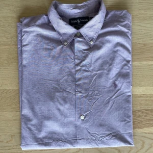Ljuslila skjorta från Ralph Lauren XL - Säljer en stilren ljuslila skjorta från Ralph Lauren i 100% bomull. Klassisk krage med knappar, diskret broderad logga på bröstet och långärmad modell. Perfekt för dig som gillar en clean och tidlös look.