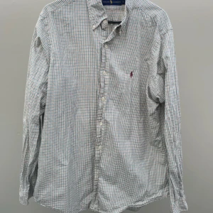 Ralph lauren skjorta - Inga defekter Klassisk rutig skjorta från Ralph Lauren i storlek L. Skjortan är vit med tunna blå och bruna rutor, har långa ärmar och knäppning framtill. Tillverkad i mjuk bomull och prydd med den ikoniska broderade loggan på bröstet.