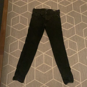 Svarta Replay Anbass jeans, stl 30 - Säljer ett par svarta Replay Anbass jeans i storlek 30. De har klassisk femficksdesign, smal passform och snyggt Replay-broderi på fickan. Jeansen är i stretchigt denim och passar perfekt till en clean och stilren look. Det finns en skada på byxorna baksidan av byxorna på grund av andvändning av skärp.