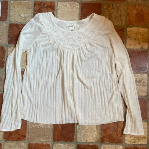 Vit tröja med spetsdetalj och lång ärm - Superfin vit tröja med långärmad design, ribbade ränder och vacker spets runt halsringningen. Luftigt material som känns skönt mot huden och ger en romantisk vibe. Perfekt att styla med jeans eller kjol för en söt look.