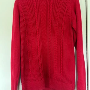 Röd stickad tröja Hampton Republic - Snygg röd stickad tröja från Hampton Republic med klassiskt flätmönster framtill. Tröjan har rund halsringning, ribbade muddar och långa ärmar. Perfekt för dig som gillar en stilren och tidlös look. Sitter som en XS/S bara snvänd en enda gång!