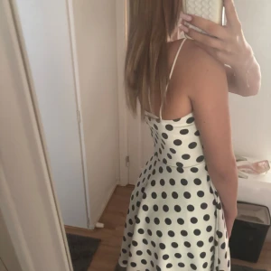 Vit prickig kortklänning med tunna band - Den är sååå fin!!Supersöt vit kortklänning med svarta prickar och tunna axelband. Klänningen har v-ringning och ärmlös design, perfekt för varma dagar. Materialet känns slätt och svalt, troligtvis polyester eller liknande. Den har en klassisk och lekfull look som sticker ut.