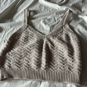 Beige stickad linnetopp med mönster - Säljer en beige stickad linnetopp med breda axelband och snyggt strukturmönster i zickzack. Toppen är croppad och har ribbad kant nedtill, perfekt för en chill och trendig look. Supermjuk och passar till allt från jeans till kjol.