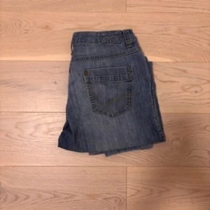 Blå raka jeans med cargoficka - Säljer ett par blå jeans med raka ben och en extra cargoficka på ena benet. Klassisk femficksmodell med bälteshällor och dragkedja. Jeansen har en avslappnad passform och är tillverkade i denim. Perfekta för en chill och casual stil.