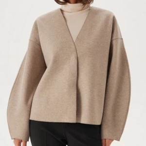 Beige omlott cardigan jacka - Stilren beige cardigan jacka med omlott-design och v-ringad hals. Jackan har en loose passform och långa ärmar, perfekt för lager-på-lager. Tillverkad i mjukt ullmaterial som ger en clean och modern look. Den är slutsåld!!🥰