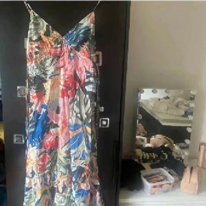 Blommig långklänning med smala axelband - Färgstark långklänning med blommigt mönster i blått, rött, rosa, grönt och gult. Klänningen har smala axelband, v-ringning och en luftig passform. Perfekt för varma dagar och ger en riktigt somrig vibe.