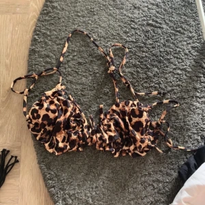 Leopardmönstrad bikiniöverdel med snörning - Snygg bikiniöverdel med leopardmönster i bruna och svarta toner. Modellen har rynkade kupor och tunna snören som knyts i nacken och ryggen. Perfekt för dig som vill sticka ut på stranden i sommar.