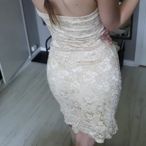 Guldig spetsklänning - Säljer en superfin kort klänning i guld färgad spets. Lite Serena Wanderwoodsen vibes. Tubmodell utan axelband och figurnära passform som framhäver siluetten. Klänningen har vacker spets över hela och en lätt vågig kant nertill. Perfekt för dig som vill sticka ut med en elegant look. Står inte storlek men skulle säga S.