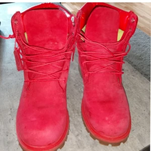 Röda Timberland boots  - Snygga röda Timberland boots i mocka med klassisk snörning och grov sula. Skorna har rund tå och detaljer i rött läder vid ankeln. Perfekta för dig som vill sticka ut med färg i höst och vinter.