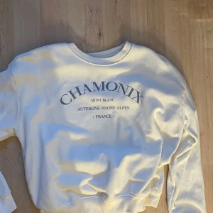 Vit sweatshirt Chamonix print - Vit sweatshirt med tryck i mörkblått där det står 'CHAMONIX' och text om Mont Blanc och Frankrike. Tröjan har rund halsringning, långa ärmar och ribbade muddar. Perfekt för en chill och sportig look.