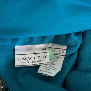 Turkos paljettklänning från Invito - Superfin turkos kortklänning från Invito med glittriga paljetter och blommigt mönster. Klänningen har breda axelband med volangdetaljer och korsad rygg. Tillverkad i polyesterblandning med stretch för en bekväm passform. Perfekt för dig som vill sticka ut!