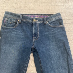 Mörkblå jeans från Soft Touch - Snygga mörkblå jeans från Soft Touch med klassisk femficksdesign och kontrastsömmar. Insidan har lila detaljer och logga. Jeansen har normal passform. 