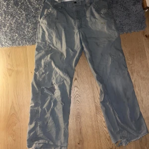 Carhartt byxor - Riktigt snygga grå carhartt byxor hål i ena knät, små fläckar på framsidan och patchen på baksidan är borta. Pågrund av allt detta säljer jag dom billigt.