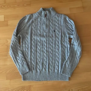 Grå quarter zip - Snygg grå kabelstickad tröja i storlek M. Tröjan är aldrig använd.