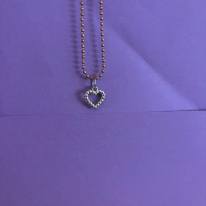 Halsband med hjärthänge i silver - Sött halsband med kulkedja i guldton och ett hjärthänge i silverfärg. Hänget är format av små kulor som bildar ett hjärta, vilket ger en trendig och lekfull look. Perfekt accessoar för att lyfta din outfit med en touch av kärlek.