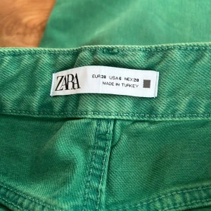 Gröna jeansbyxor från Zara, strl 38 - Snygga gröna jeansbyxor från Zara i klassisk femficksmodell. Byxorna har hög midja och raka ben, tillverkade i bomull med en skön känsla. Perfekta för dig som vill sticka ut med färg i vardagen.