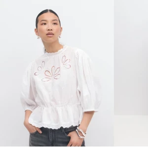 Vit blus med broderade detaljer - Superfin vit blus med broderade blommor och hålbroderi framtill. Blusen har puffiga trekvartsärmar, volangkant nertill och söt spets vid halsen. Perfekt för dig som gillar romantisk och luftig stil.