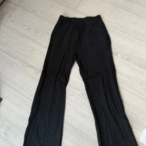 Svarta vida linnebyxor - Svarta linnebyxor med avslappnad passform och raka, vida ben. Byxorna har resår i midjan och är tillverkade i ett lätt och luftigt linnematerial, perfekta för en chill och stilren look.