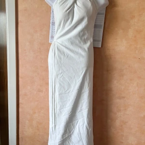  Plisserad veckad halter klänning öppna ryggen  - Säljer en elegant vit långklänning med draperad överdel och plisserad detalj längs ena sidan. Klänningen är axelbandslös och har en stilren, figurnära passform som ger en snygg siluett. Perfekt för dig som vill sticka ut med en klassisk look.