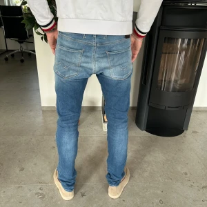 Replay Anbass ljusblå jeans slim fit - Snygga ljusblå Replay Anbass jeans med slim fit och klassisk femficksdesign. Jeansen har diskreta slitningar framtill, ljus tvätt och detaljerade sömmar på bakfickorna. Tillverkade i mjuk bomullsdenim med stretch för extra komfort.