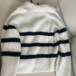 Randig stickad tröja med half zip - Vit och svart randig stickad tröja med krage och half zip-dragkedja framtill. Tröjan har långa ärmar och är ribbstickad för en mysig och trendig look. Perfekt för en clean look