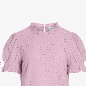 Ljusrosa blus med broderade detaljer - Supersöt ljusrosa blus från Vila med broderade hålmönster och puffiga korta ärmar. Blusen har liten volang vid halsen och ärmarna, samt knapp i nacken.  Köpt från bubbelroom för 299, och endast använd fåtal gånger.
