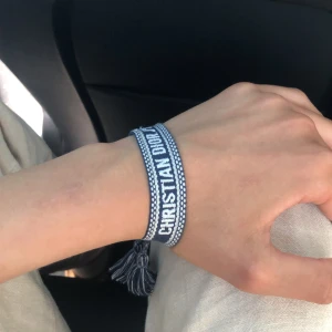 Blått Christian Dior J'Adior armband - Snyggt blått tygarmband från Christian Dior med texten 'CHRISTIAN DIOR J'ADIOR' broderad i vitt. Armbandet har justerbar knytning och coola tofsar i ändarna. Perfekt accessoar för att lyfta din outfit med en lyxig touch. Passar till allt och är perfekt för sommaren!!✅✅