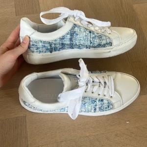 Sneakers från 3'Belles i vitt och blått - Snygga sneakers från 3'Belles med vit skinnfront och sidor i blåmelerad textil. Skorna har breda vita snören, guldfärgade öljetter och en klassisk rund tå. Perfekt för dig som gillar en unik och fräsch look med mix av material. Köpte dom utomlands för runt 1100kr men dom har tyvärr inte kommit till andvändning 