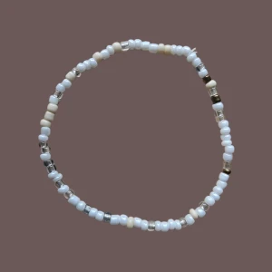 Pärlarmband i vitt och silver - Ett stilrent armband med små pärlor i vitt, beige och silver. Pärlorna är trätt på en elastisk tråd och ger en enkel men trendig look.