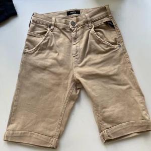 Beige shorts från Replay - Snygga beige shorts från Replay med klassisk femficksdesign och uppvikta benslut. De har normal passform, bälteshällor och knappgylf. Materialet är mjuk bomull som känns skönt mot huden. Perfekta för varma dagar när du vill ha en clean och stilren look.