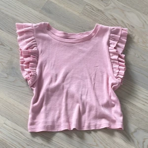 Rosa volangtopp från UNIQ YOUNG - Supersöt knappt använd rosa topp från UNIQ YOUNG med volangdetaljer på axlarna. Toppen är ärmlös och har en mjuk, skön känsla i bomull. Perfekt för dig som gillar en gullig och trendig stil med extra detaljer på axlarna.