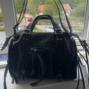 Svart väska från bherska  - Bherskas ”Bowling bag”. Cool svart handväska från Bershka i skinnimitation med flätade handtag och justerbar axelrem. Väskan har dragkedja upptill, en ficka med dragkedja framtill och snygga metalldetaljer. Perfekt för dig som vill ha en stilren och rymlig väska med edge. Helt ny och aldrig använd med lappen kvar. 