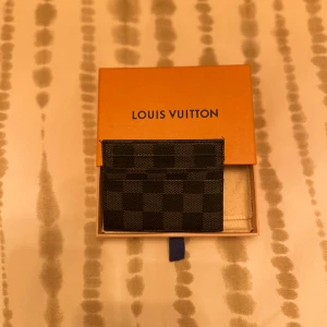 rutmönstrad korthållare - Säljer en stilren svart korthållare  med klassiskt rutmönster. Den är tillverkad i tåligt skinn och har flera fack för kort. Perfekt accessoar för dig som vill ha något både snyggt och praktiskt i fickan.