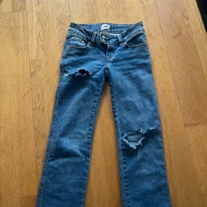 Blå bootcut jeans med slitningar - Snygga blå jeans från 157 med bootcut passform och slitna detaljer på båda benen. Klassisk femficksmodell med låg midja och dragkedja. Perfekta för dig som gillar en avslappnad och trendig look.