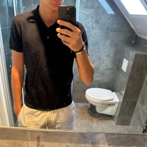 Marinblå pikétröja från Zara - Klassisk svart pikétröja från Zara i storlek M. Tröjan har korta ärmar, krage och knäppning framtill med två knappar. Snygg och enkel modell som passar perfekt till jeans eller shorts. Materialet känns mjukt och bekvämt mot huden.