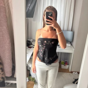 Svart tubtopp med broderi - Svart tubtopp från Hennes Collection med blomtryck i rosa och beige. Toppen har fransar längs nederkanten